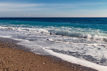 The waves of the Mediterranean sea roll on the pebble beach in clear weatherの写真素材