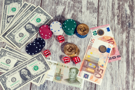 Colorful casino chips, dollars, bitcoins and red dice lie on a light wooden tableの写真素材
