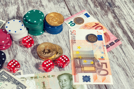 Colorful casino chips, dollars, bitcoins and red dice lie on a light wooden tableの写真素材