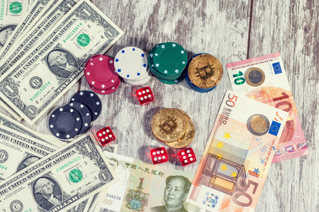 Colorful casino chips, dollars, bitcoins and red dice lie on a light wooden tableの写真素材