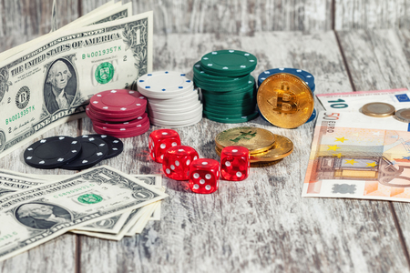 Colorful casino chips, dollars, bitcoins and red dice lie on a light wooden table .On the dice fell all four unitsの写真素材