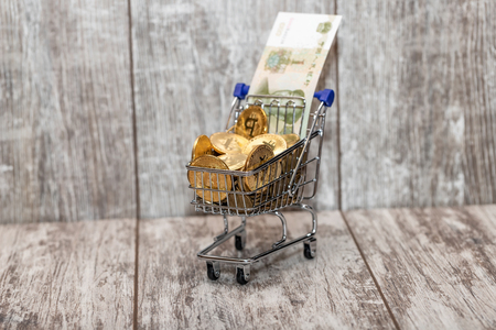 A metal toy cart from the supermarket is filled to the top with gold coins bitcoin and 1 yuan billの写真素材