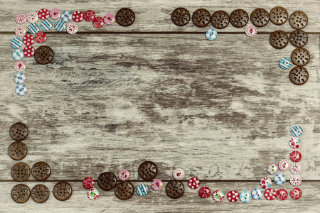 Buttons of different shapes and colors are laid out on a light wooden background at the edges with an empty space under the inscription in the center . The concept of handmade sewing.の写真素材