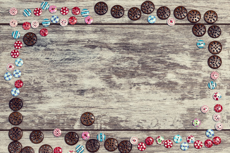 Buttons of different shapes and colors are laid out on a light wooden background at the edges with an empty space under the inscription in the center . The concept of handmade sewing.の写真素材