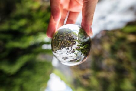 Rapid rapid mountain waterfall among the pine forest. The picture was taken through a crystal ballの写真素材