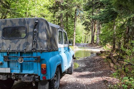 Old reliable jeep of high cross-country standing in front of a puddle in the forest with high pinesの写真素材