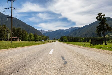 The old asphalt road goes away against the background of the great Caucasus mountains and high fluffy cloudsの写真素材