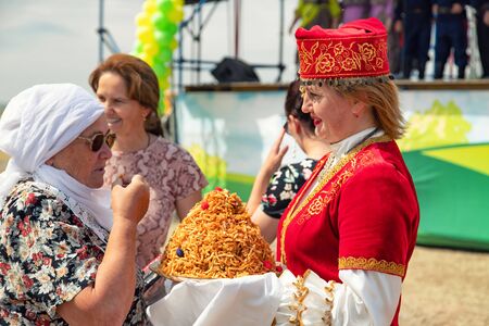 VOLGOGRAD, RUSSIA - JUNE 8: Girls dressed in national costumes treat all guests to traditional Sabantuy sweets. June 8, 2019 in Volgograd, Russia.のeditorial素材