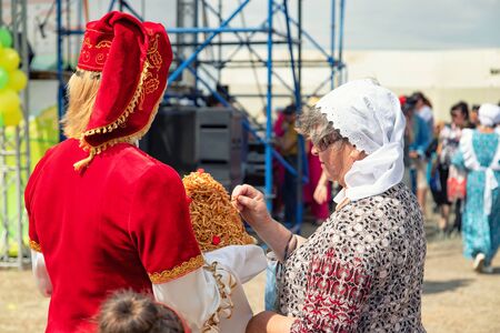 VOLGOGRAD, RUSSIA - JUNE 8: Girls dressed in national costumes treat all guests to traditional Sabantuy sweets. June 8, 2019 in Volgograd, Russia.のeditorial素材
