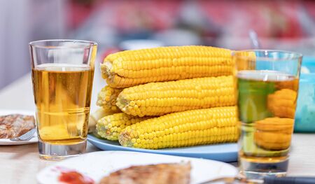 Light dinner for two : Boiled corn on the cob, roasted meat and beer in glassesの写真素材