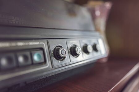An old vinyl record player with a wooden case stands on a chest of drawers of the same era. Close-up volume and frequency controlsの写真素材