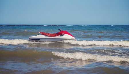 Red and white jet ski splashing on the waves near the shore.の写真素材