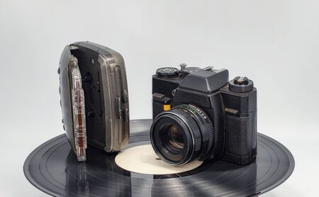 An audio cassette player with a cassette and an old film camera stand on a black vinyl recordの写真素材