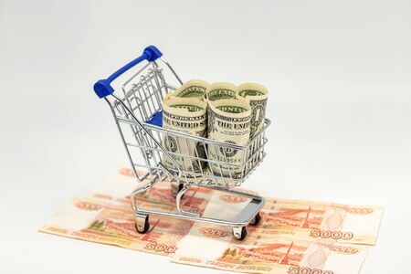 There are rolled-up dollars in a toy grocery cart. The cart rides on ruble billsの写真素材