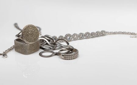 Different in shape silver rings with cubic Zirconia, silver bracelet and chain with elegant weaving on white reflect surfaceの写真素材