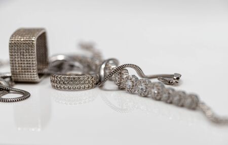 Different in shape silver rings with cubic Zirconia, silver bracelet and chain with elegant weaving on white reflect surfaceの写真素材