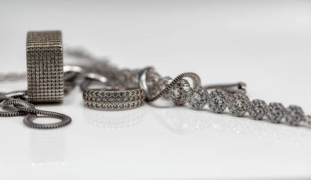 Different in shape silver rings with cubic Zirconia, silver bracelet and chain with elegant weaving on white reflect surfaceの写真素材