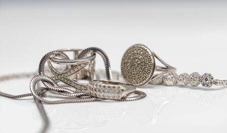 Different in shape silver rings with cubic Zirconia, silver bracelet and chain with elegant weaving on white reflect surfaceの写真素材