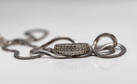 Delicate silver diamond ring and silver chain with elegant design on white acrylicの写真素材