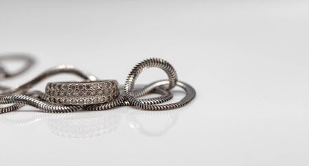 Delicate silver diamond ring and silver chain with elegant design on white acrylicの写真素材