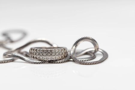 Delicate silver diamond ring and silver chain with elegant design on white acrylicの写真素材