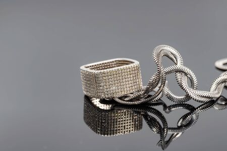 Square silver diamond ring and silver snake chain on black reflective surfaceの写真素材