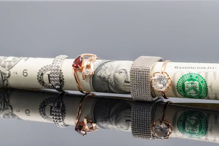 The rolled-up one-dollar bill wears silver and gold rings