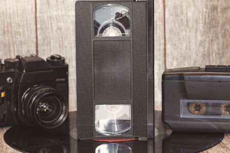 Technique of the 90s : audio cassette player, film camera and VHS cassette on a wooden background