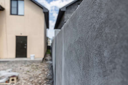 A stucco-lined fence wall against the background of a new beige country houseの写真素材