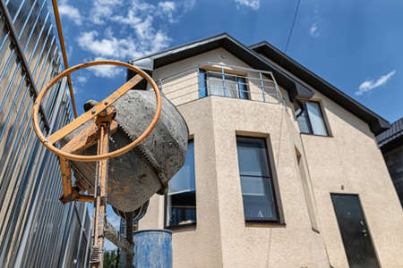 An old concrete mixer, a shovel and a pile of sand against the background of a small cozy cottageの写真素材
