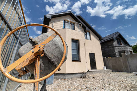 An old concrete mixer, a shovel and a pile of sand against the background of a small cozy cottageの写真素材