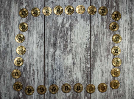 A frame of gold bitcoin coins is laid out on a wooden background. Background of the day of writing a...