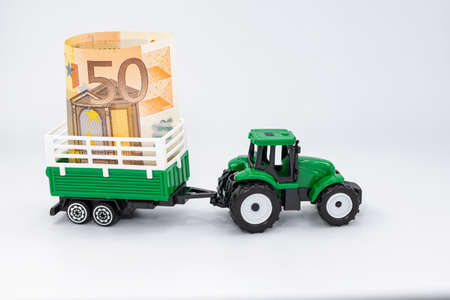 A toy farm tractor carries a 50 Euro banknote in a trailerの写真素材