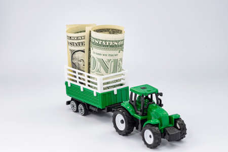 Green toy tractor carries dollars in a trailerの写真素材