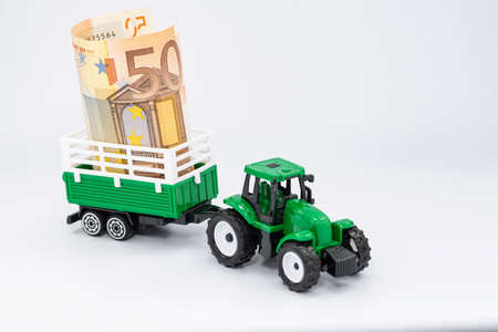 A toy farm tractor carries a 50 Euro banknote in a trailerの写真素材
