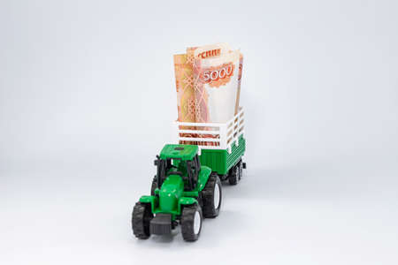 A toy green farm tractor carries five-thousand-ruble bills rolled into a tube in a trailerの写真素材