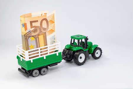 A toy farm tractor carries a 50 Euro banknote in a trailerの写真素材