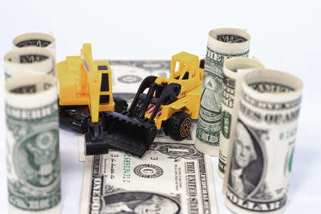 Toy construction bulldozer loads money into the back of a toy truck