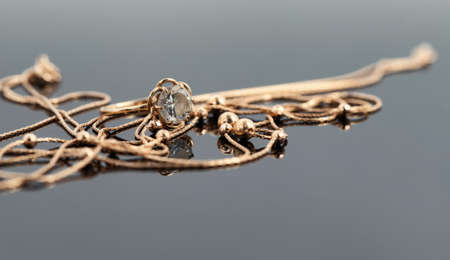 A gold ring with a large gemstone and a gold chain necklace lie on a dark reflective surfaceの写真素材