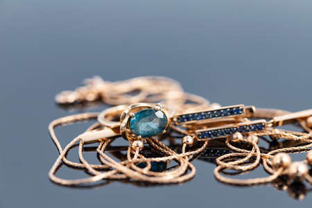 A gold chain with a pendant, earrings and a Topaz ring lie on a dark reflective surfaceの写真素材