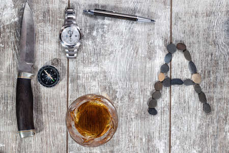 Men's items and accessories lie on a light wooden background. The letter A of the English alphabet is made of small stonesの写真素材