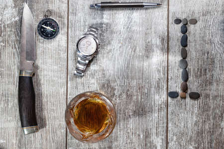 Men's items and accessories lie on a light wooden background. The letter I of the English alphabet is made of small stonesの写真素材