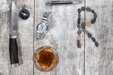 Men's items and accessories lie on a light wooden background. The letter R of the English alphabet is made of small stonesの写真素材