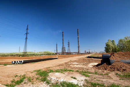 Large diameter plastic pipes lie on the ground against the backdrop of a large oil refineryの写真素材