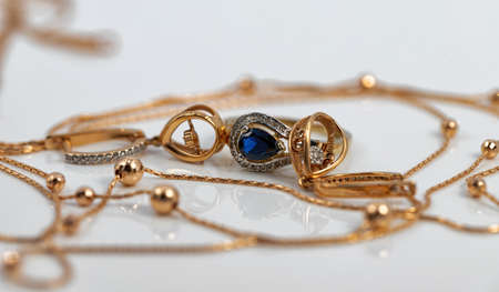 A gold chain with a pendant, earrings and a Topaz ring lie on a dark reflective surface