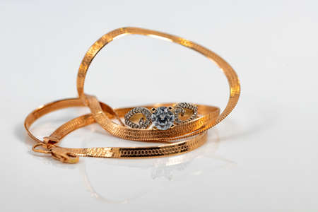 A gold chain with a snake skin weave and a large diamond ring are reflected on the white surfaceの写真素材