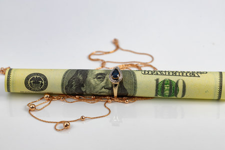 A hundred dollar bill rolled into a tube and inserted into a gold ring with a sapphire