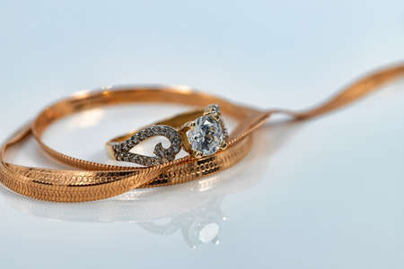 A gold chain with a snake skin weave and a large diamond ring are reflected on the white surfaceの写真素材