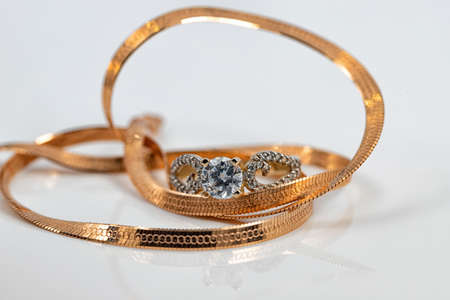 A gold chain with a snake skin weave and a large diamond ring are reflected on the white surfaceの写真素材