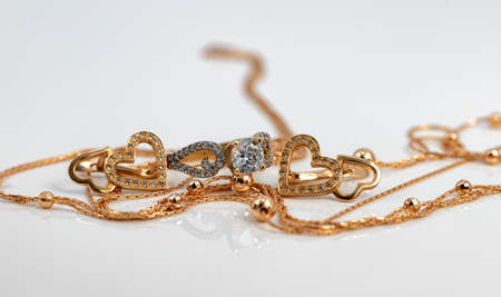 A gold chain with a pendant, earrings and a diamond ring lie on a dark reflective surfaceの写真素材